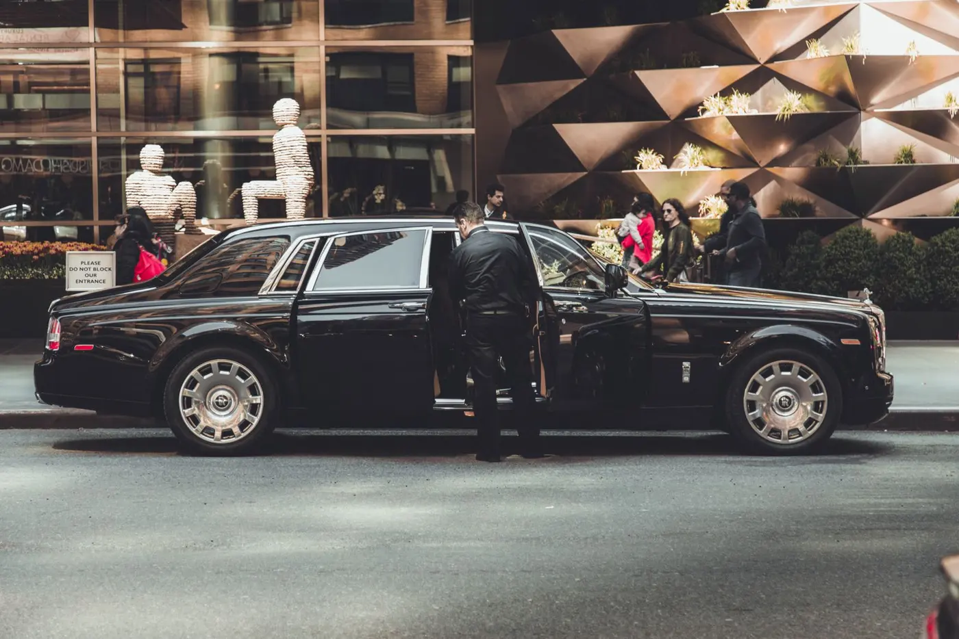 Chauffeur holding the door of a black limousine at a city entrance